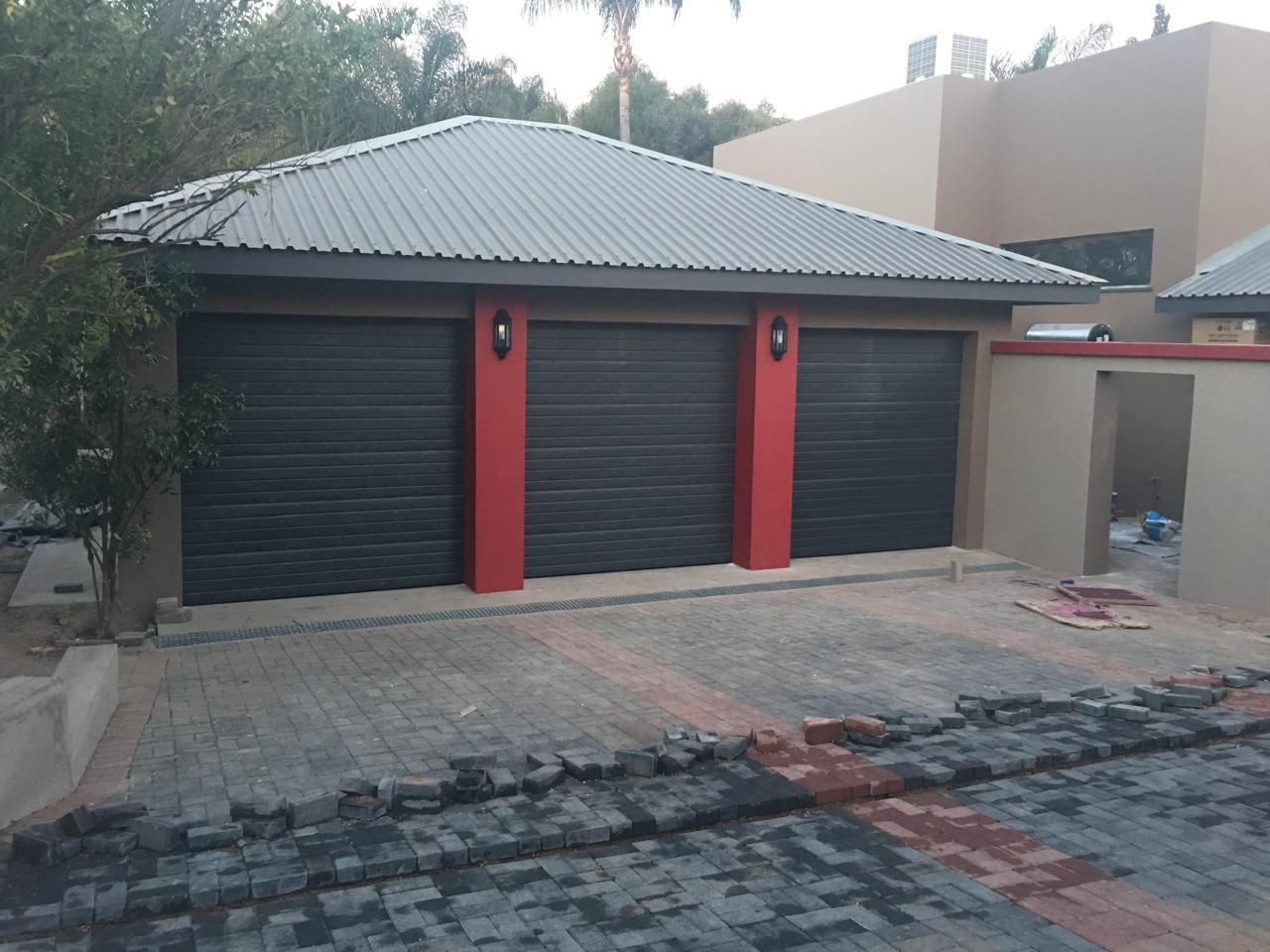 Three separate dark garage doors with red dividing columns